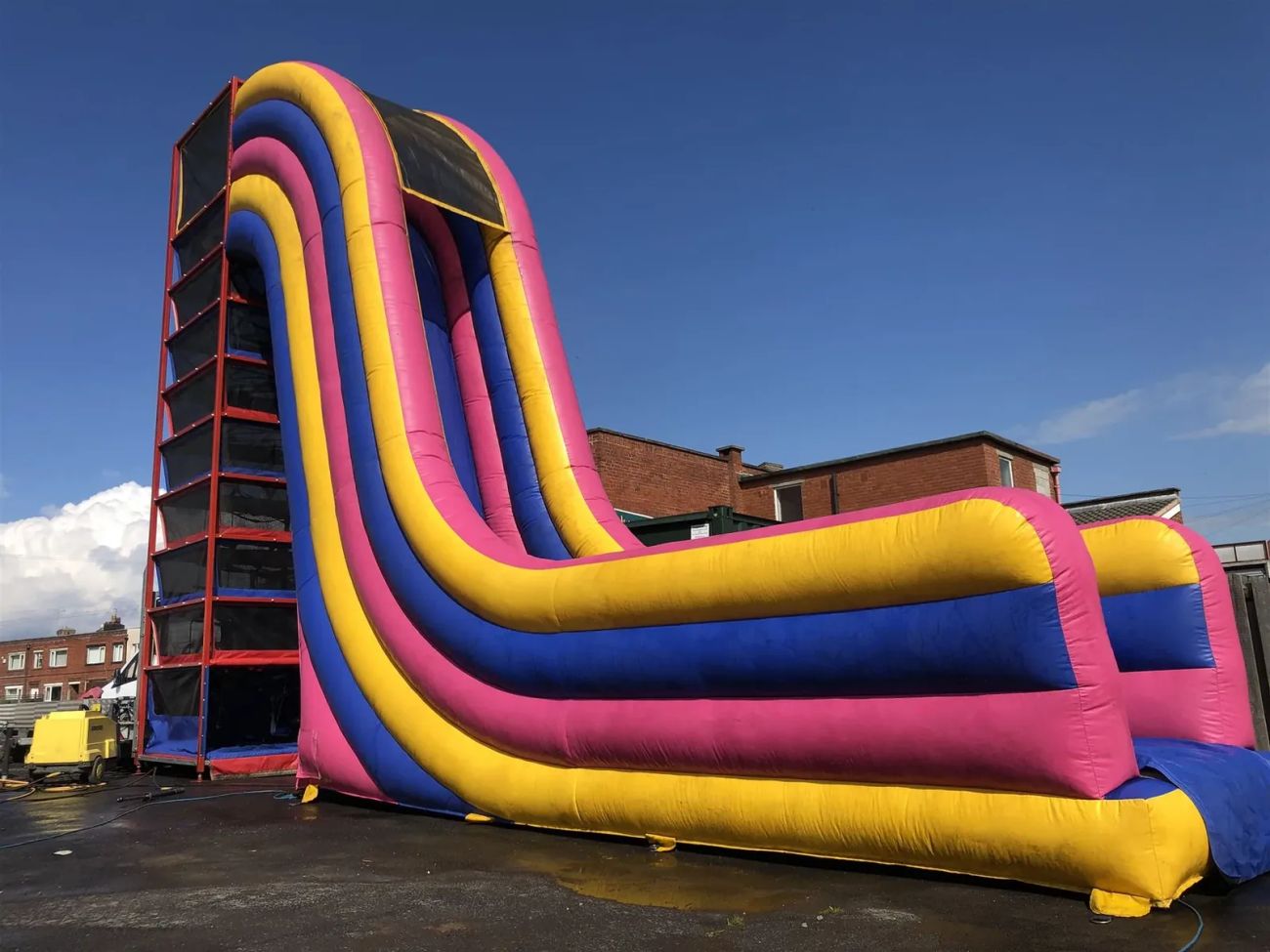 Tall red infinity climbing tower beside a large pink, blue and yellow inflatable mega drop slide