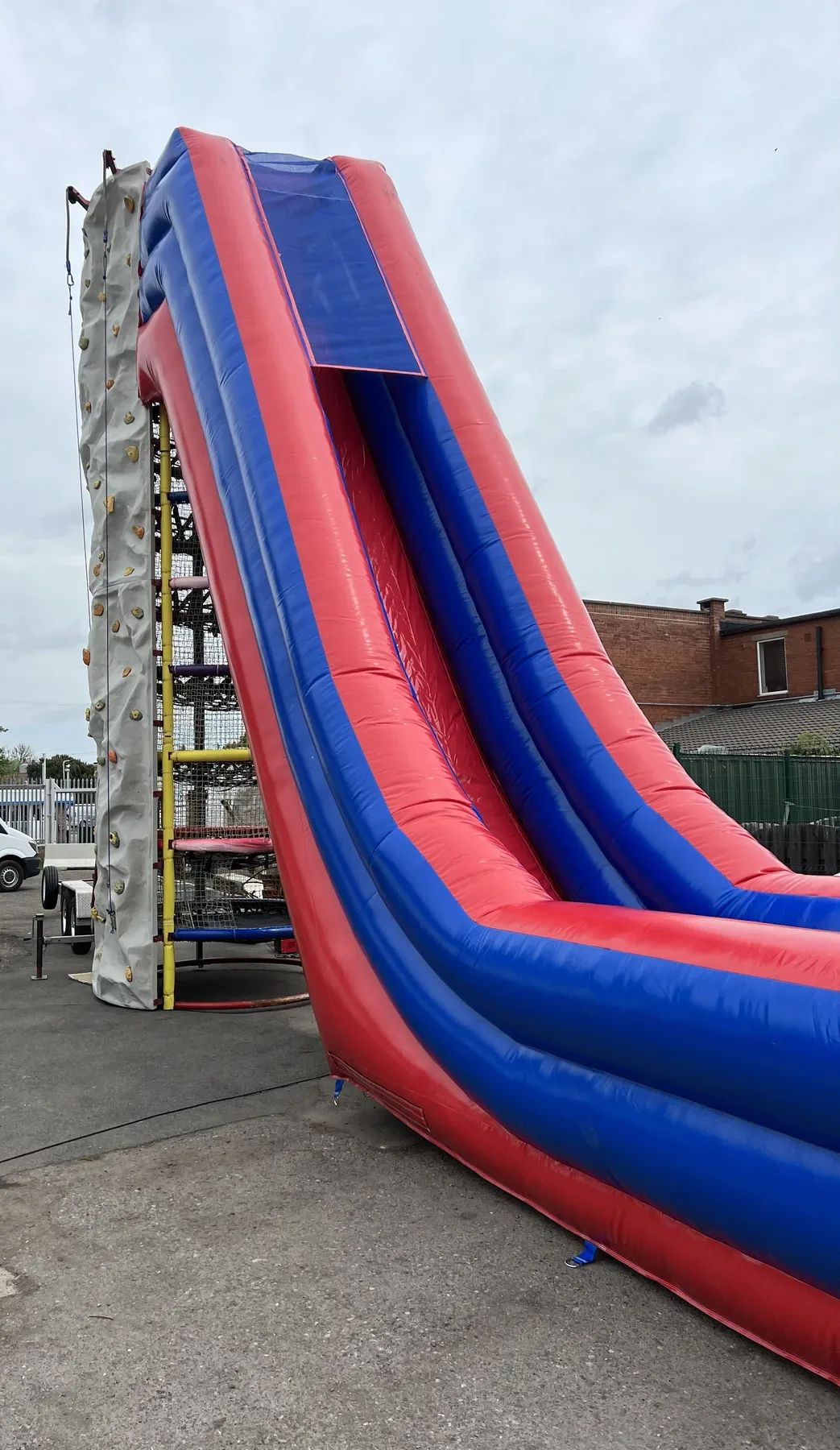 Tall outdoor climbing wall with a red and blue inflatable dual slide attached