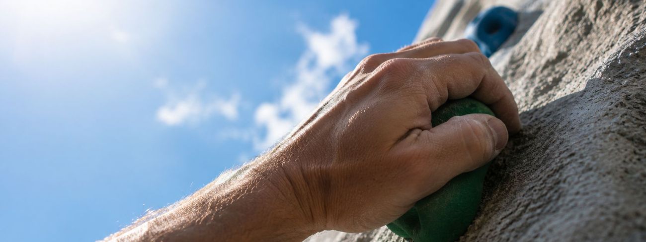 Close-up of a climber's hand gripping a green hold on a mobile climbing wall