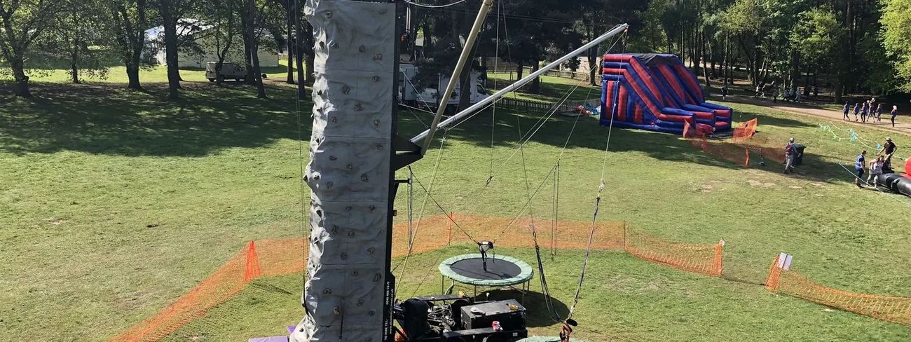 Mobile climbing wall with bungee trampolines set up on a grassy outdoor event field