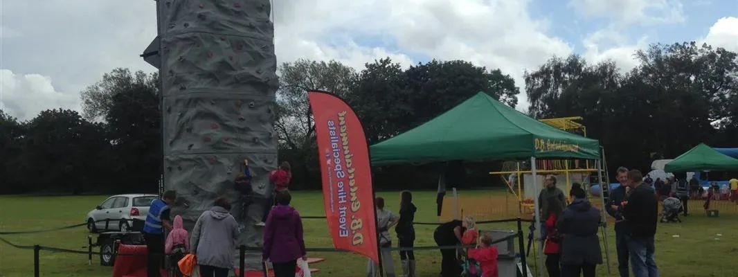 Tall grey mobile climbing wall at an outdoor event with children climbing and adults watching nearby