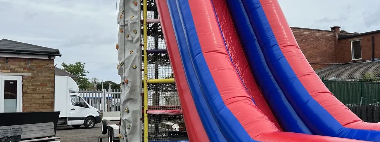 Spider Mountain with grey climbing wall and red and blue mega drop slide set up outdoors